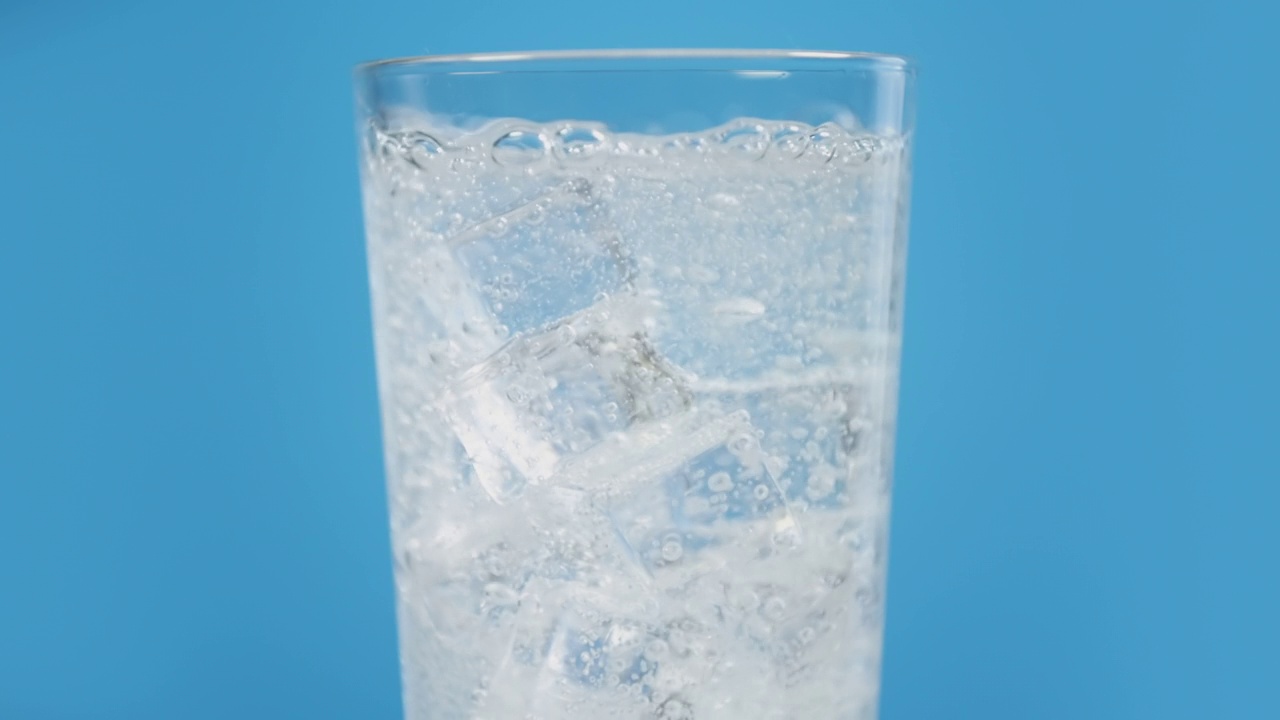 玻璃杯里装满冰冷的气泡水，配上蓝色背景的冰块，透明的碳酸饮料视频素材