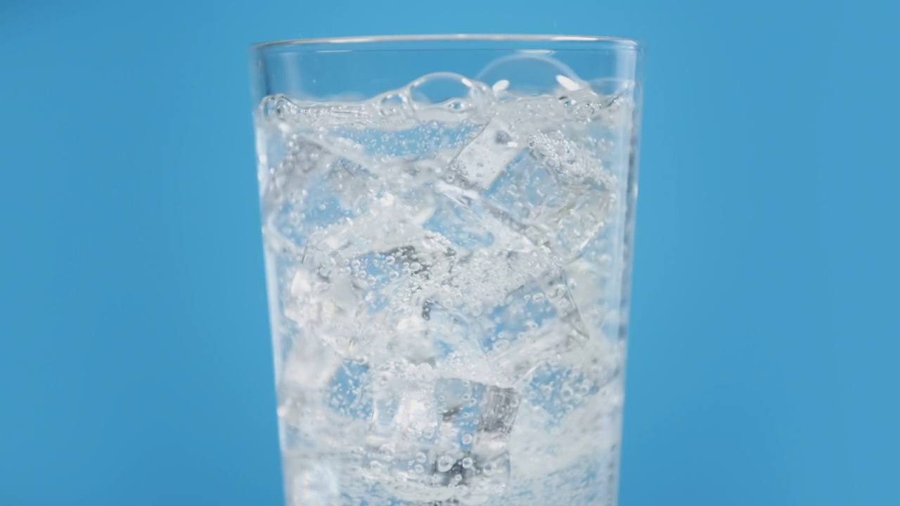 玻璃杯里装满冰冷的气泡水，配上蓝色背景的冰块，透明的碳酸饮料视频素材