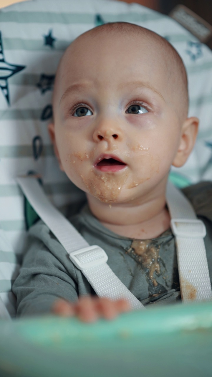 可爱的宝宝在孩子的餐椅上吃饭，脸上沾满了食物视频下载