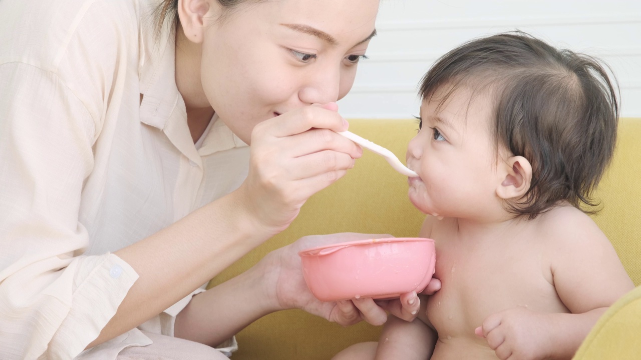 年轻的母亲用勺子喂女儿吃东西。视频下载
