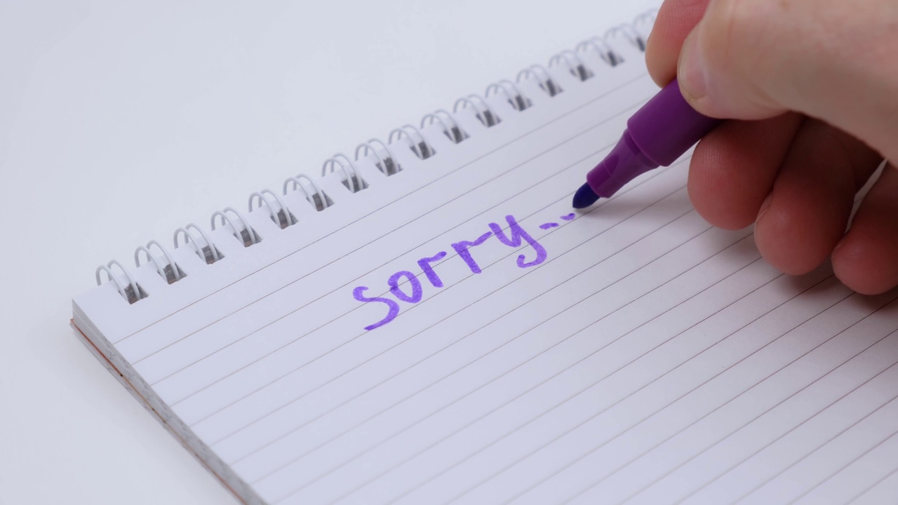 男士用紫色马克笔在笔记本上写下“对不起”。关闭了。视频下载