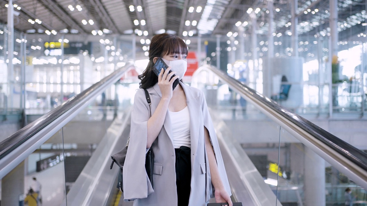 亚洲女商人戴着口罩在机场航站楼的自动扶梯上打电话视频素材