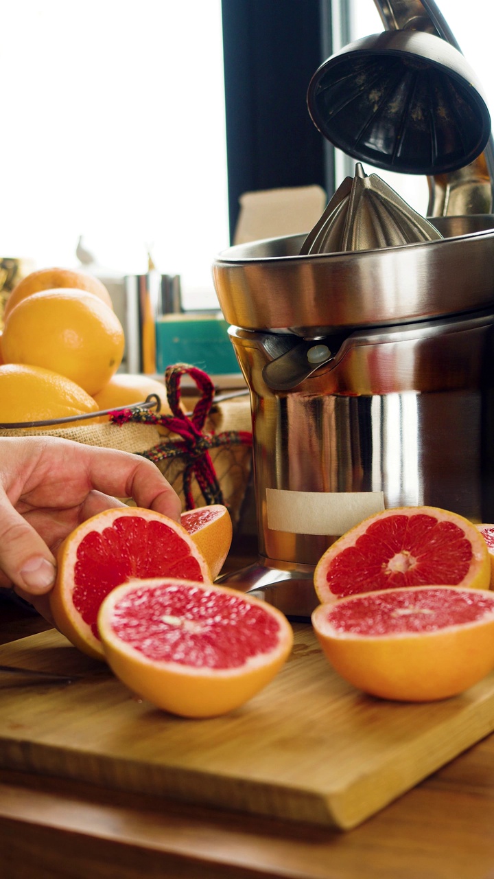 垂直的画面。男性的手正在榨汁机前切柚子。健康食品和素食主义。视频素材