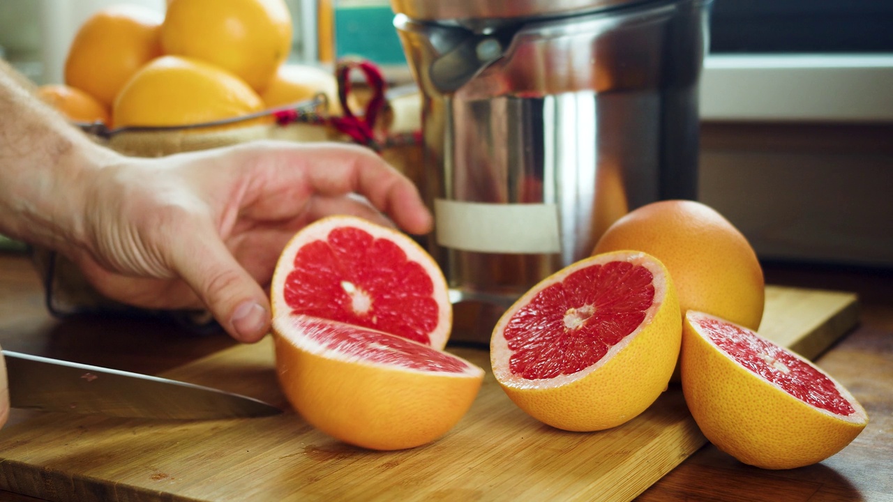 健康饮食和素食主义——一名男子为榨汁机切葡萄柚。视频素材