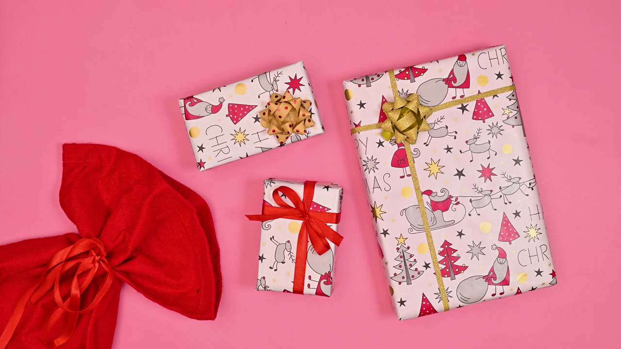 圣诞礼物出现在粉红色背景的红色圣诞老人包里。平的。停止运动视频下载