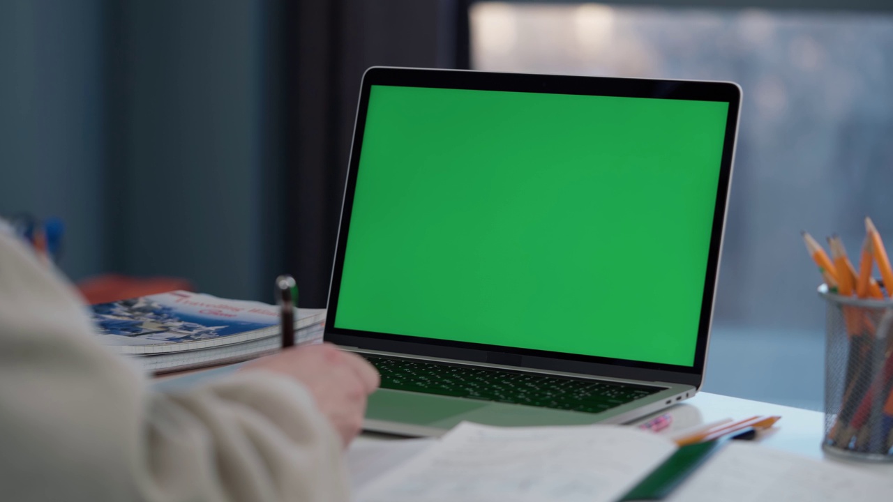 一名女子使用绿色屏幕的笔记本电脑。女孩在笔记本上记笔记视频素材