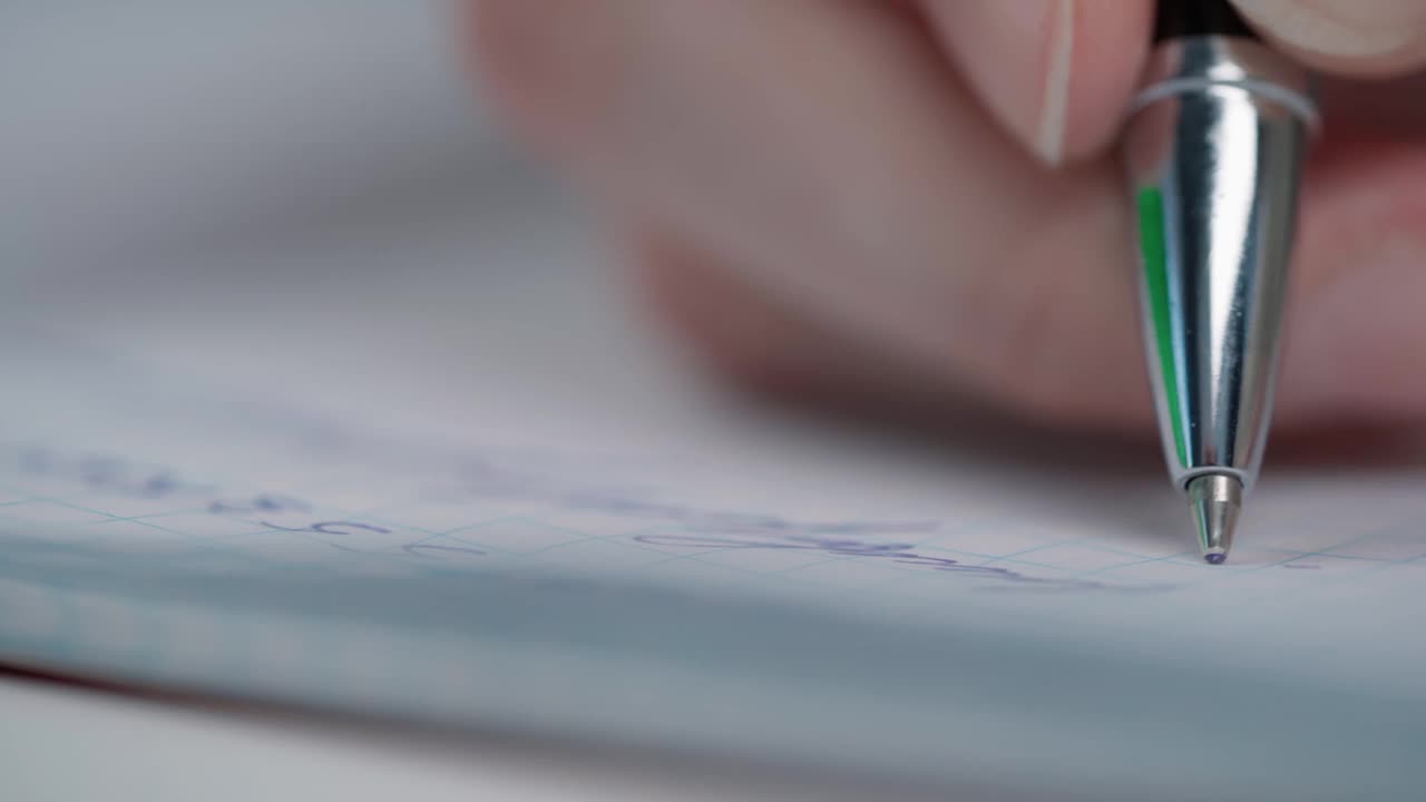 从笔记本电脑上的女性用笔在纸笔记本上写字的特写视频素材