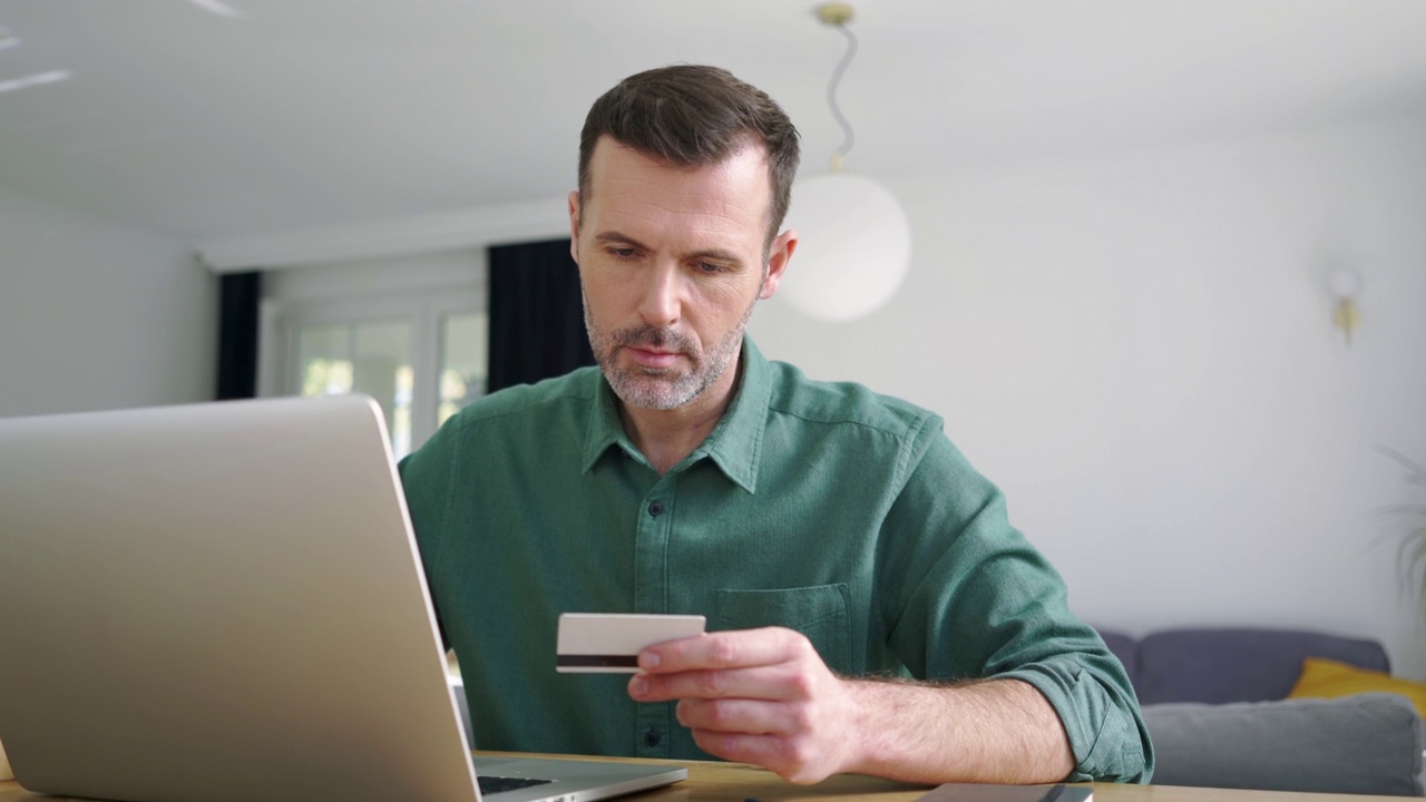 一名男子在家用笔记本电脑用信用卡在线支付视频素材