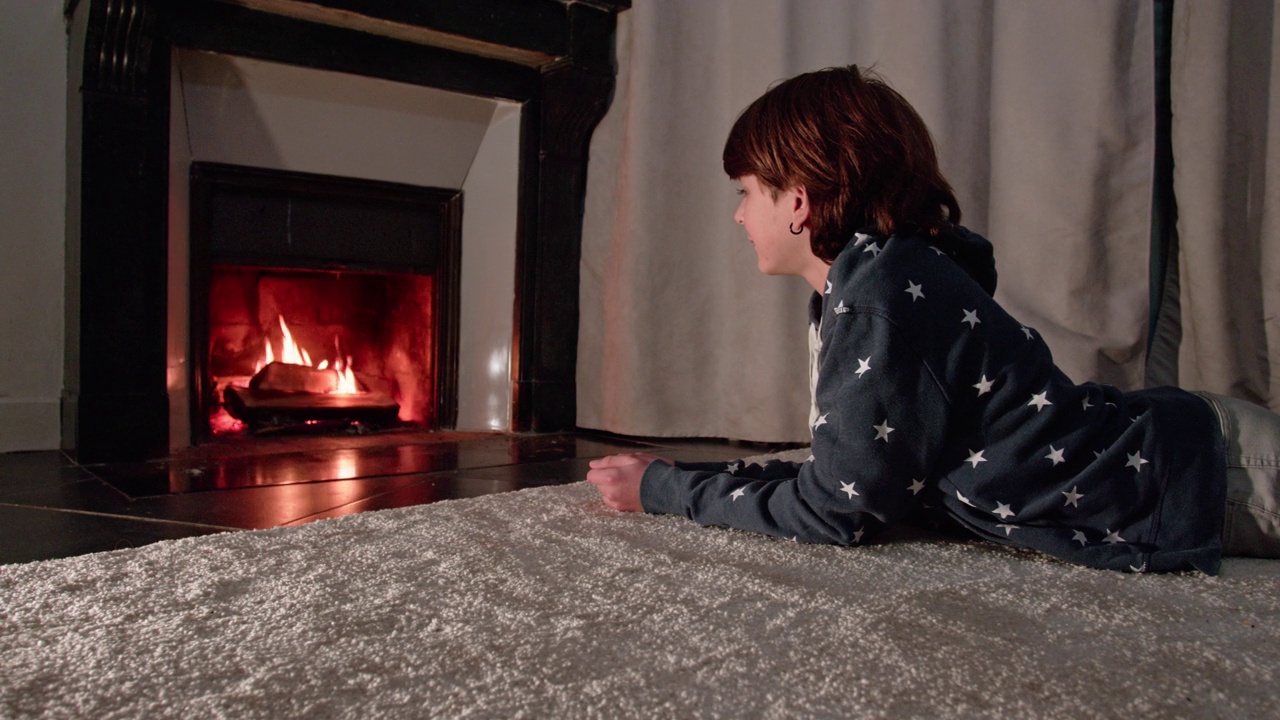 年轻英俊的男孩坐在壁炉前看着火视频下载