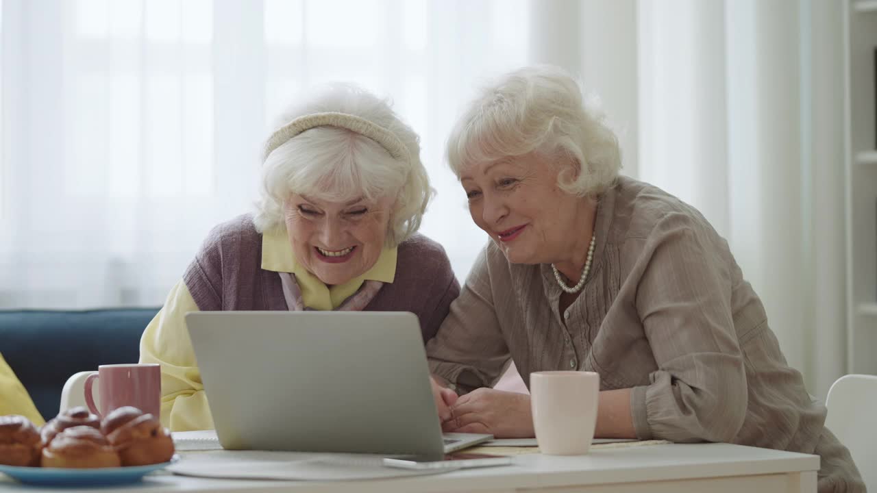 微笑的现代奶奶们对着笔记本电脑摄像头挥手，进行在线视频通话视频素材