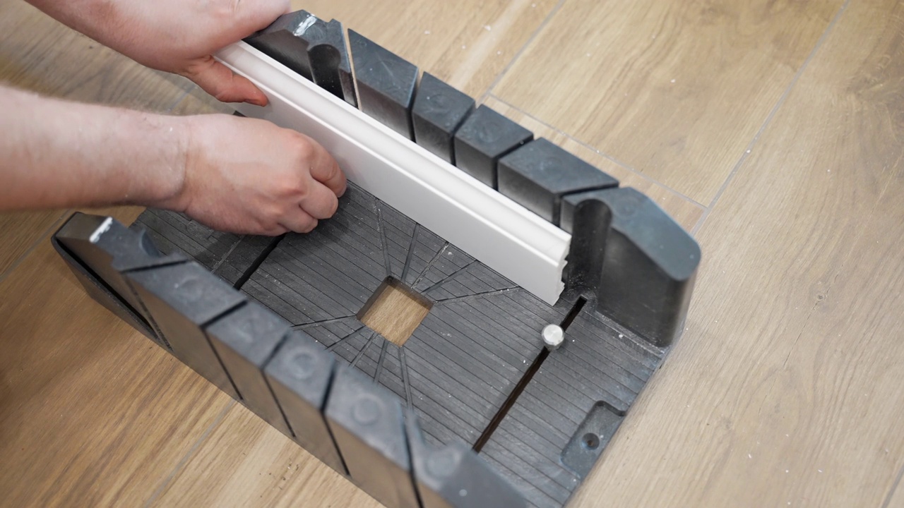 工人测量和固定白色塑料底座，用于切割和进一步安装，勤杂工使用手锯在施工现场切割踢脚板，家庭踢脚板翻新概念视频素材