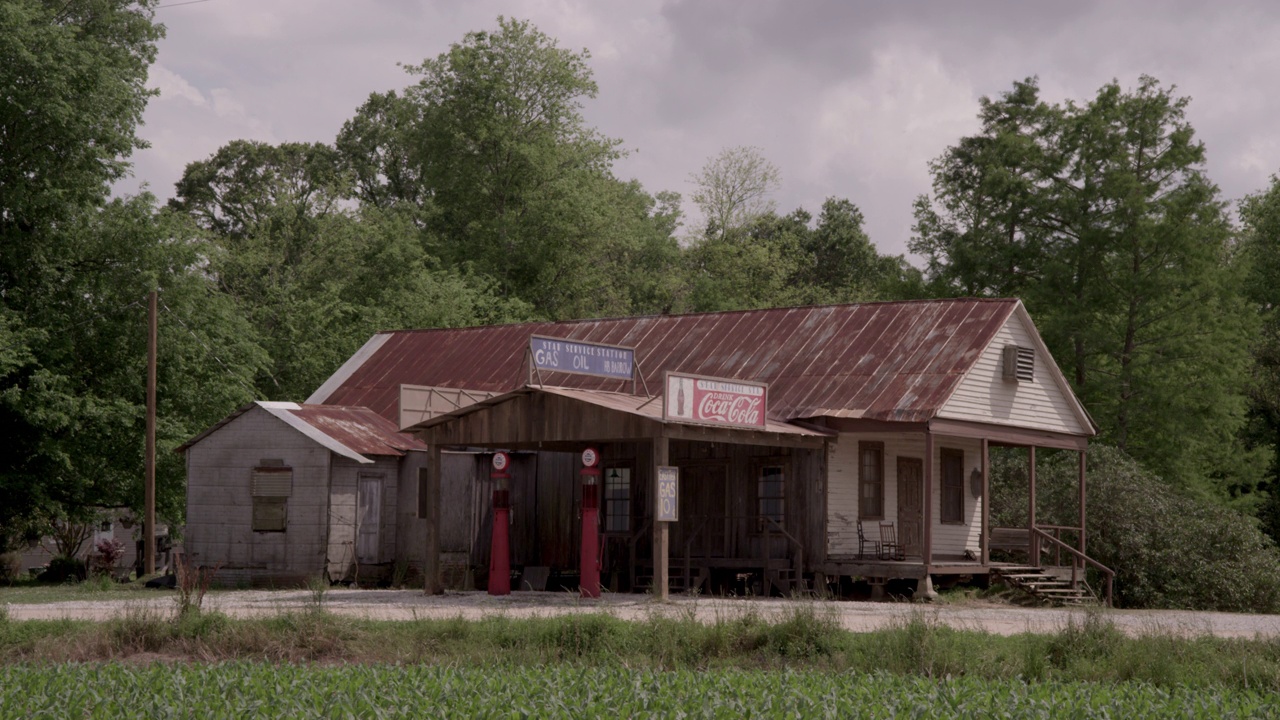 广角加油站，有可口可乐的标志，古董加油站在一个木制隔板的建筑前面。可能是一家杂货店。前景:前景中长满庄稼的田地或农田视频下载