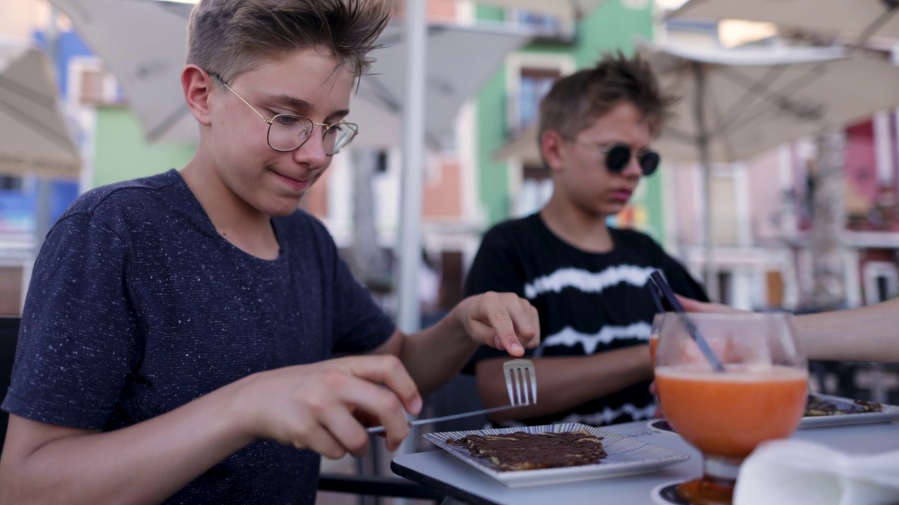 Teenage boys having crepes with chocolate in a sidewalk café视频素材