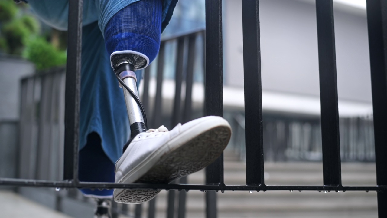 雨天，一名男子穿着假腿和白色运动鞋。一只脚踩在栅栏上视频下载