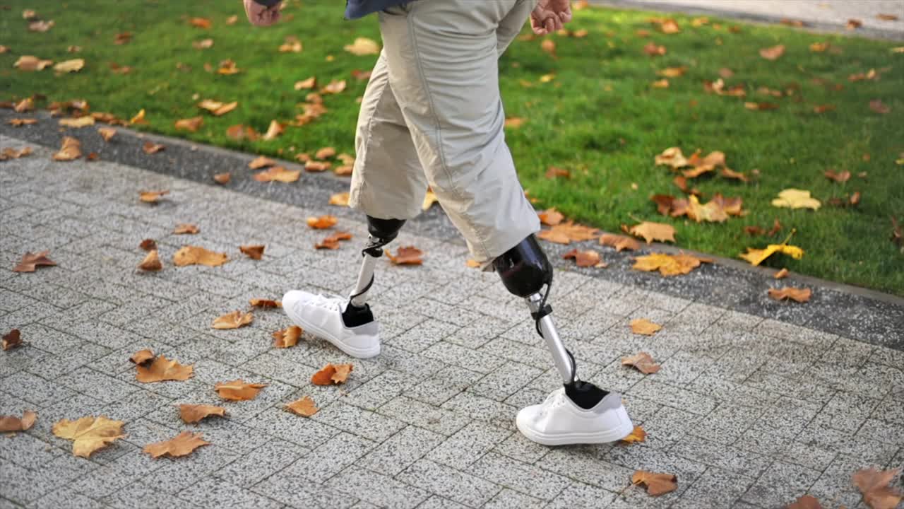 公园里一个穿着假腿和白色运动鞋走路的男人的慢镜头。地上飘落的黄叶视频下载