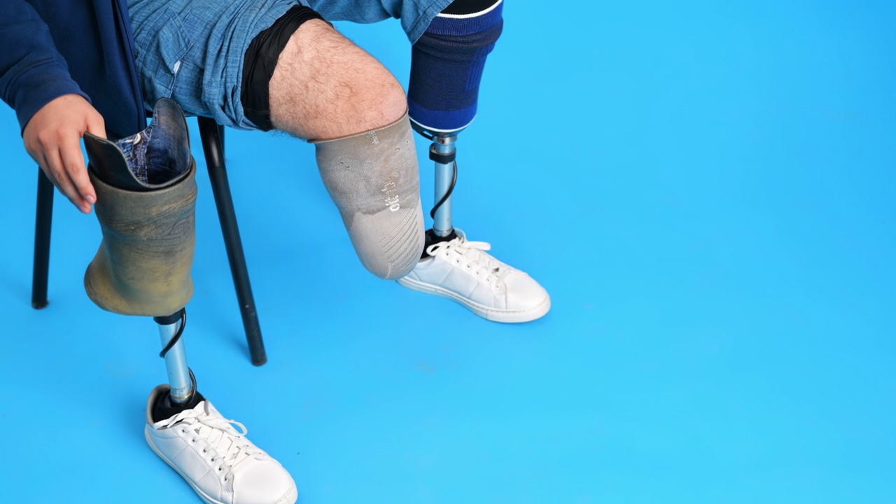 一个穿着假腿和白色运动鞋的男人。坐在椅子上取下假体，蓝色背景视频下载