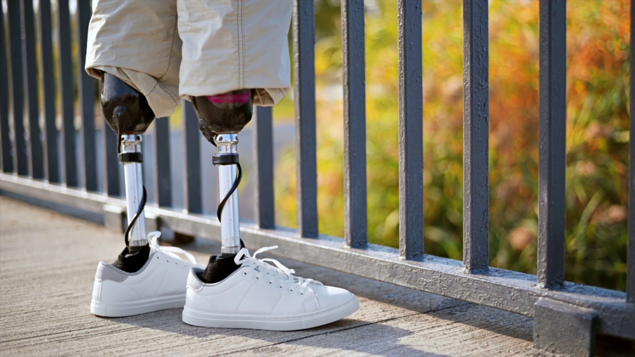一个穿着假腿和白色运动鞋的男人的慢镜头。站在栅栏旁视频下载
