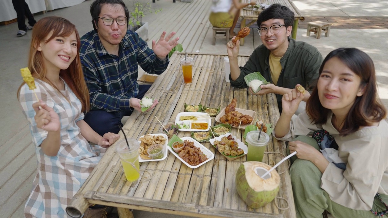 一群亚洲游客坐在一家传统餐厅里，吃着满桌的泰国食物视频下载