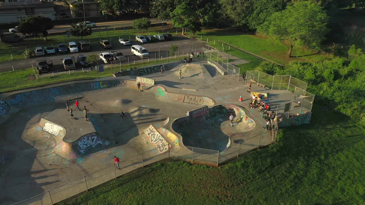 空中平移拍摄的朋友们在公园练习滑板，无人机在阳光下飞过风景——夏威夷瓦胡岛视频下载