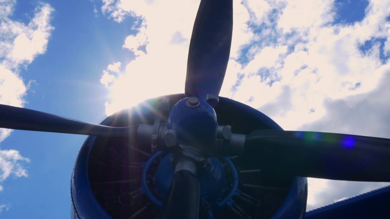 飞机的涡轮螺旋桨发动机，背景是白天蓝天白云。从下面拍摄，天顶的太阳从飞机螺旋桨涡轮后面探出来，闪闪发光视频下载