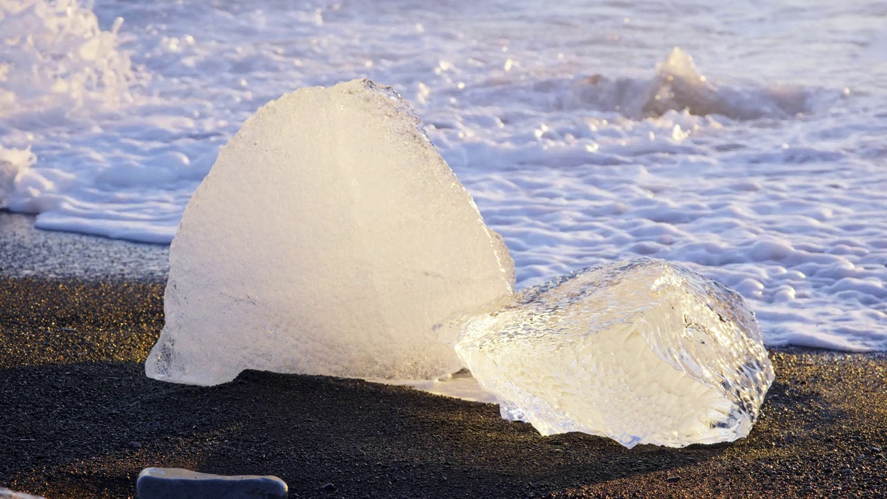 冰岛的钻石海滩，日落时冰山在黑色火山沙上闪闪发光，海浪撞击的透明冰，8K分辨率4320p拍摄视频下载