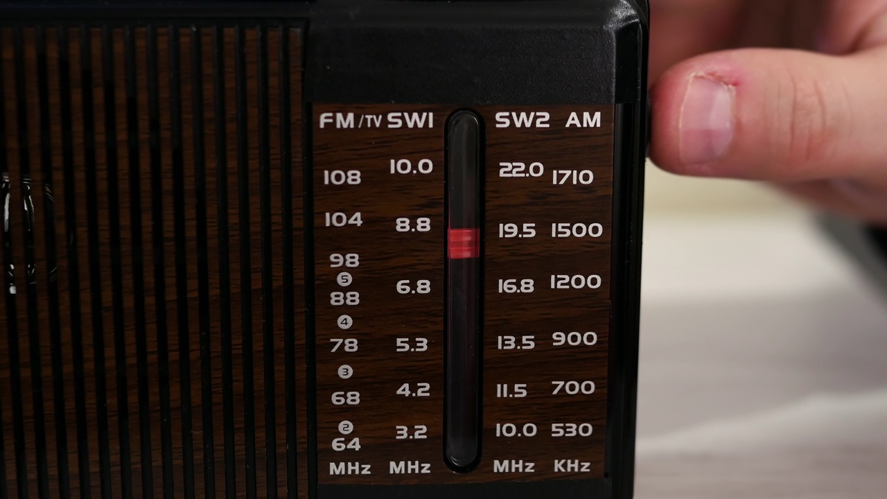 在一张旧木桌上，收音机里播放着无线电波。拧一下旧的听筒。怀旧的生活方式。把模拟收音机调到一个音阶上。一个男人在用一台旧收音机听新闻。视频素材