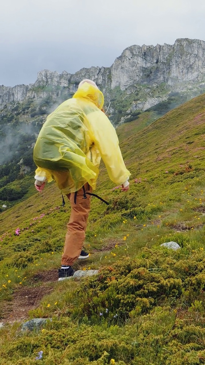 纵屏女子穿着雨衣走在山边。视频素材