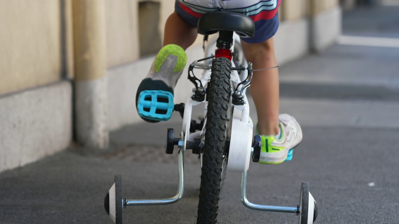 后面的孩子骑自行车与支持车轮外的城市街道人行道。接近孩子骑自行车的脚视频下载