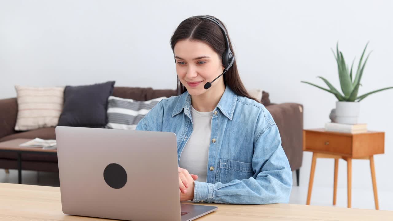 戴着耳机的年轻女性，办公室员工或呼叫中心工作人员坐在现代化的办公室里与客户交谈视频下载