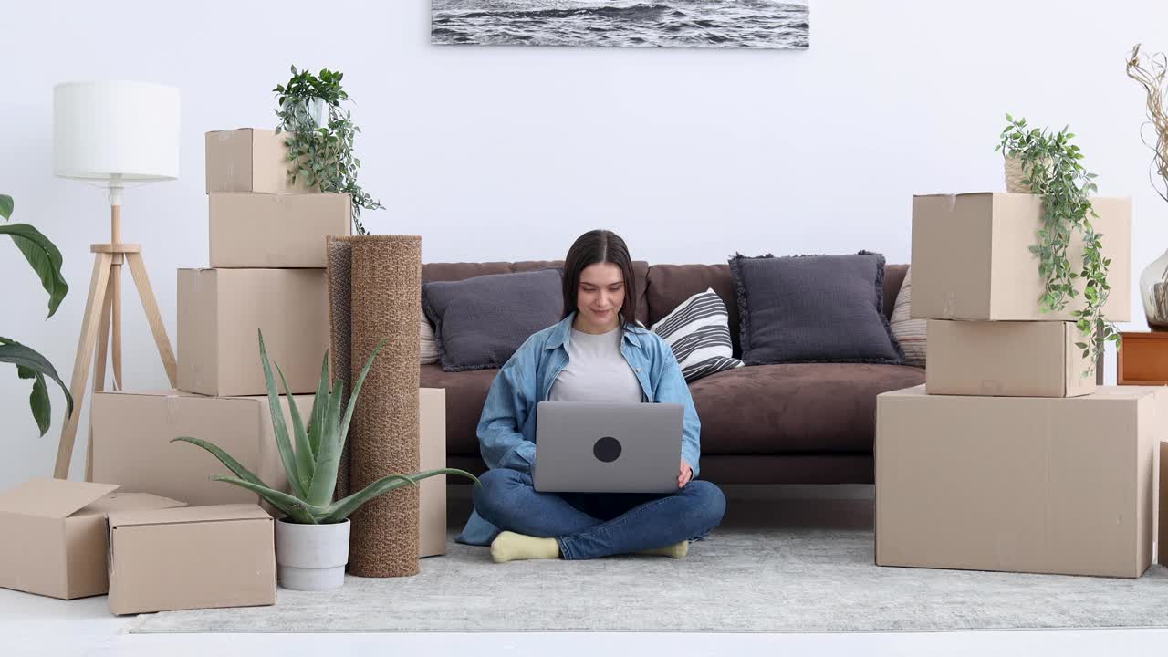 移动。快乐的年轻女子网购使用笔记本电脑坐在她的新家的地板上视频下载