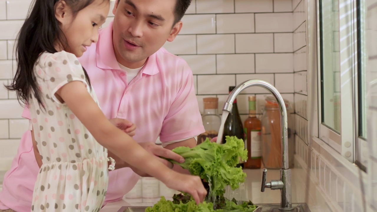 亚洲父亲教女儿在厨房水槽洗菜视频素材