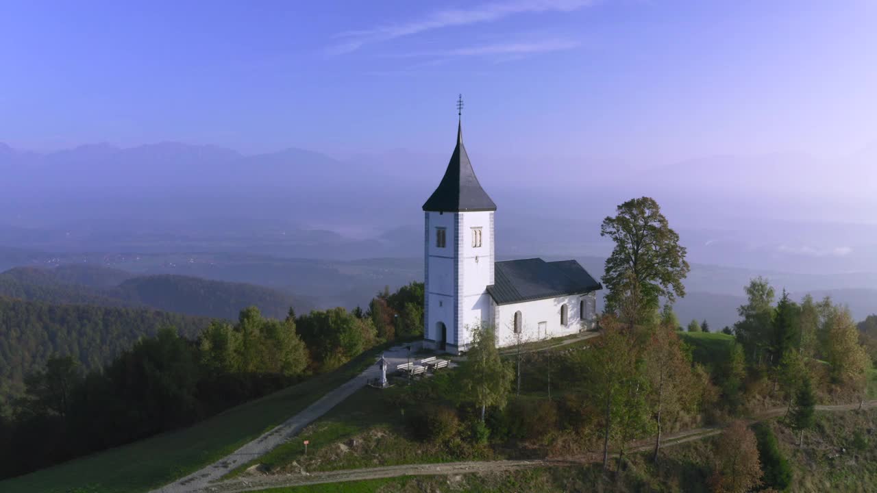 黎明时分，斯洛文尼亚山上美丽的小教堂的无人机鸟瞰图。美丽的秋日晨景视频素材