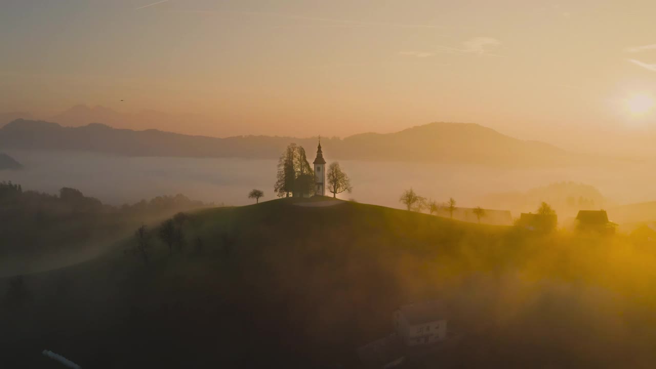 在黎明的阳光下，无人机俯瞰斯洛文尼亚山上美丽的小教堂。美丽的秋日晨景视频下载