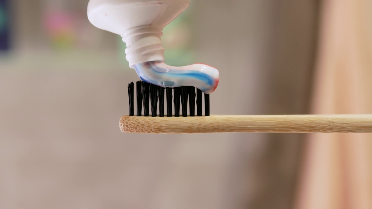 牙膏涂在牙刷上。浴室里的散景背景特写。清洁牙齿的概念。把牙膏从管子里挤出来视频素材