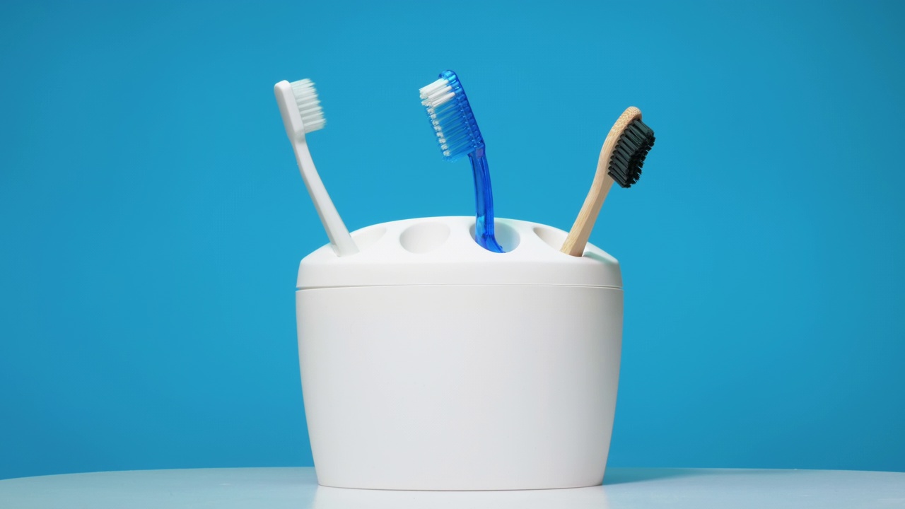 一套彩色牙刷，白色外壳，蓝色背景。牙科护理概念。牙刷定格动画。视频下载