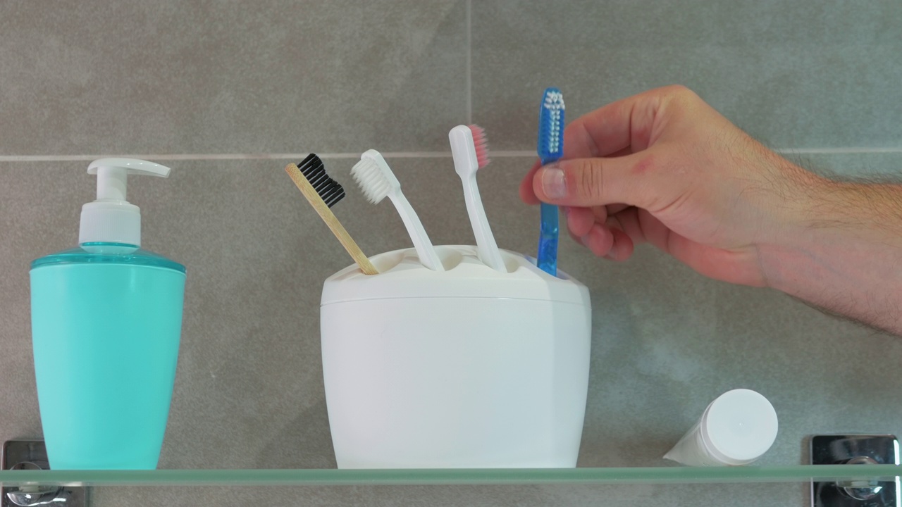一个男人的手拿着牙刷用手，白牙的概念，一个男人在浴室刷牙。白色盒子里的牙刷视频素材
