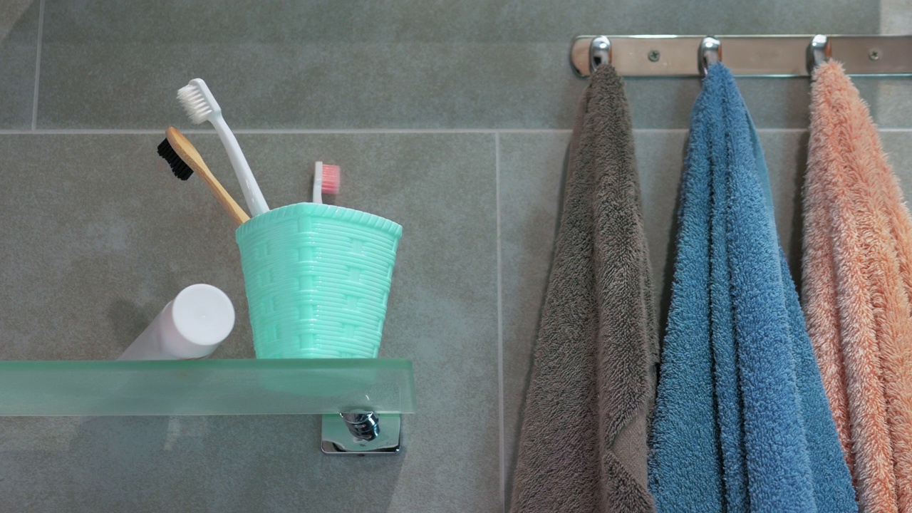 浴室里白色篮子里的牙刷的定格动画。健康牙齿的概念。浴室玻璃架子上五颜六色的牙刷。浴室里的毛巾挂在镀铬衣架上视频下载