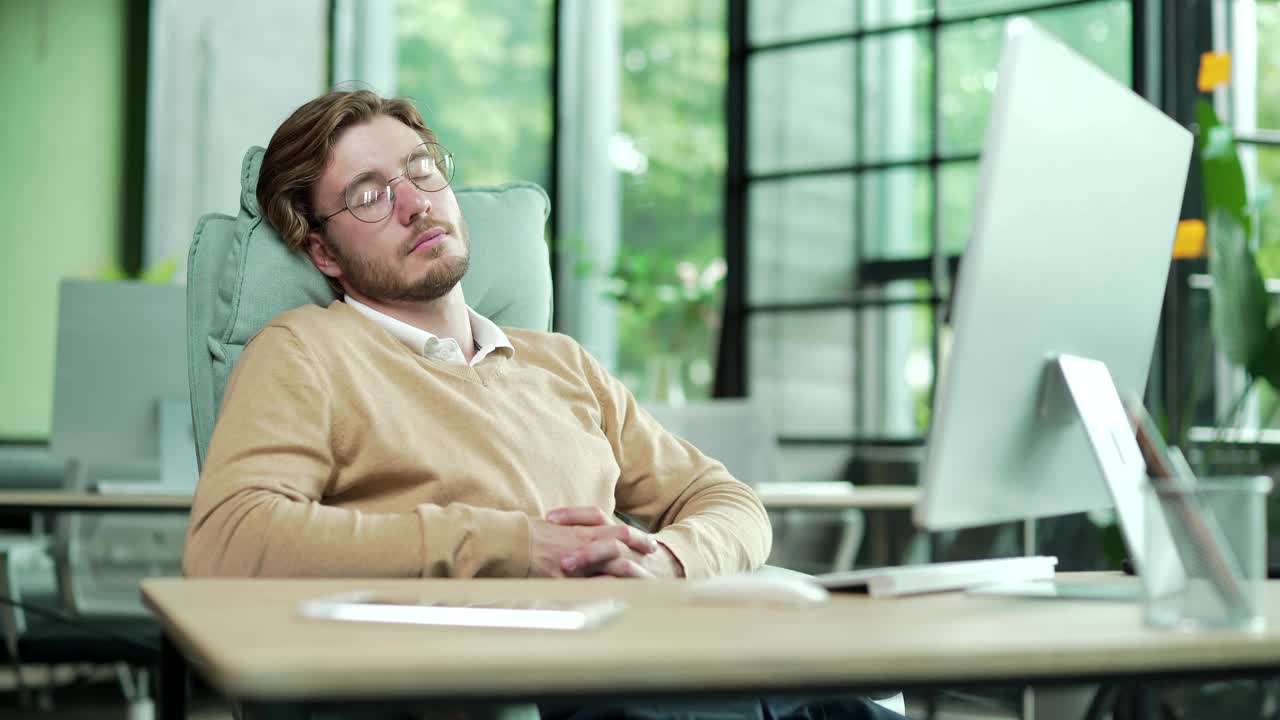 疲惫不堪的年轻办公室职员戴着眼镜在工作时间睡觉打瞌睡视频下载