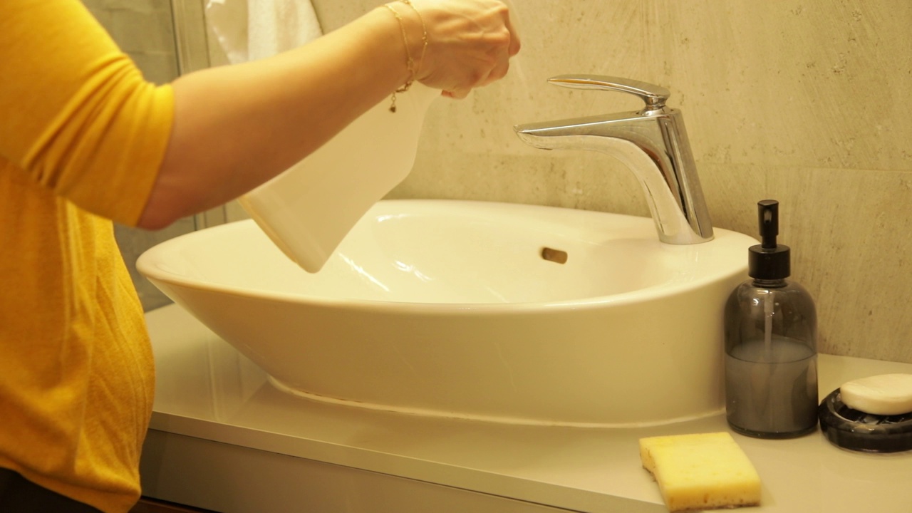 女性用手将洗洁精喷在浴室水龙头表面，然后用海绵擦洗。妇女家庭主妇在洗手间清洁脏家具。用清洁剂擦拭水槽和水龙头。清洁家居概念。视频下载