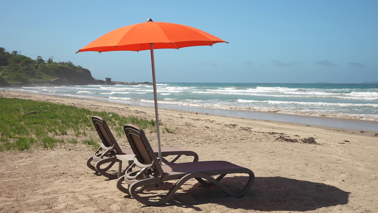 日落时分，橙色阳伞和两张躺椅躺在沙滩上。在全包酒店度假视频下载
