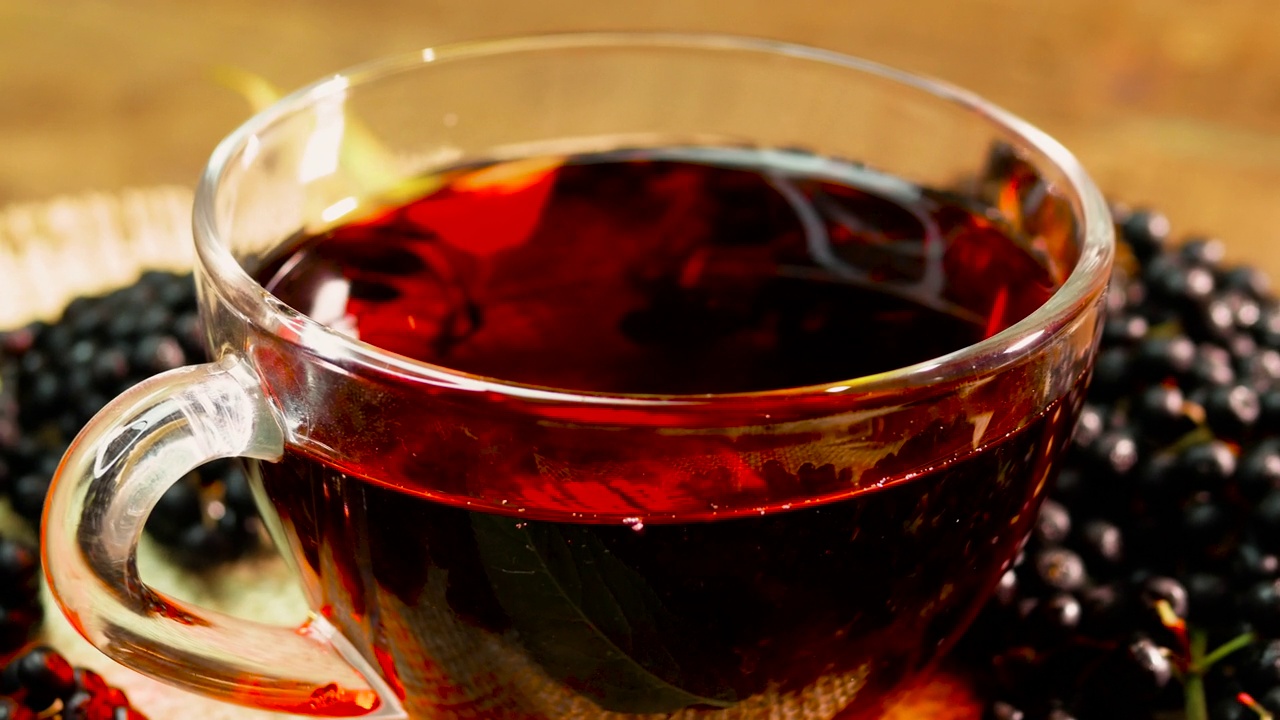 在转盘上的玻璃杯里的天然红莓茶。黑接骨木浆果茶。从浆果中挤出的顺势疗法果汁视频下载