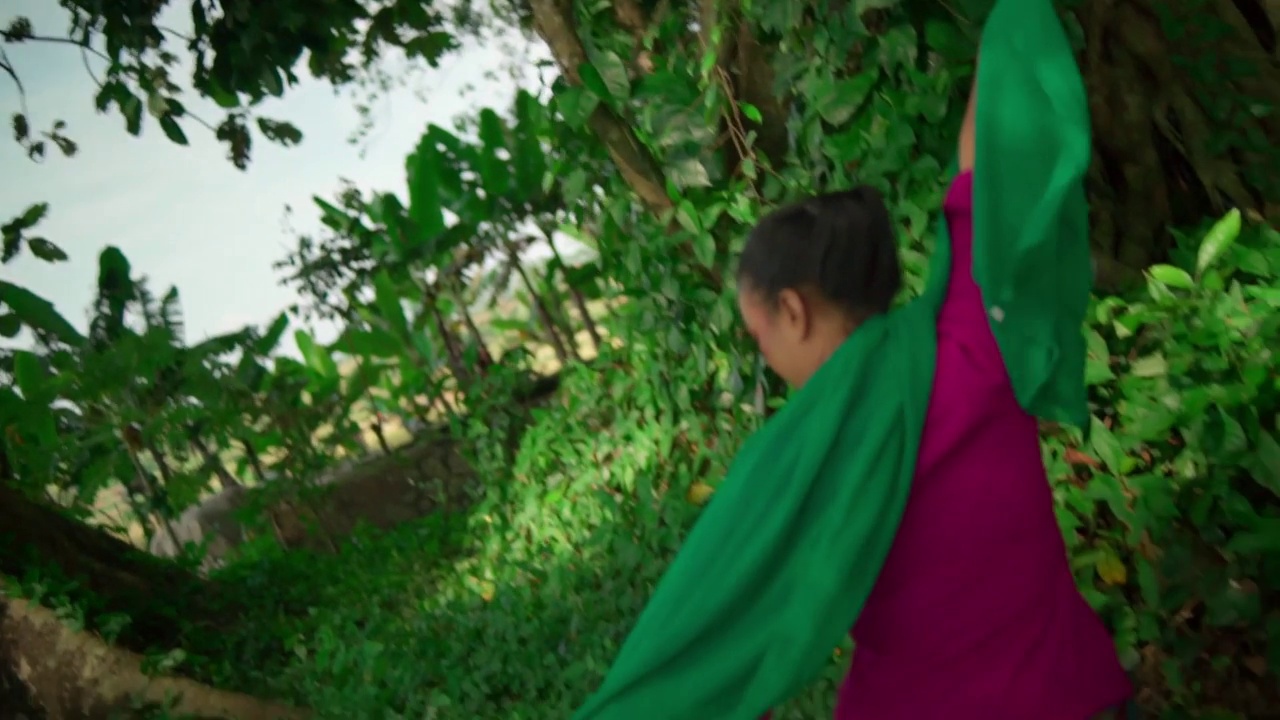一个巴厘岛女人穿着粉红色的裙子和绿色的裙子，戴着绿色的围巾在丛林中跳舞，在绿色的灌木丛中表现出兴奋的表情视频素材