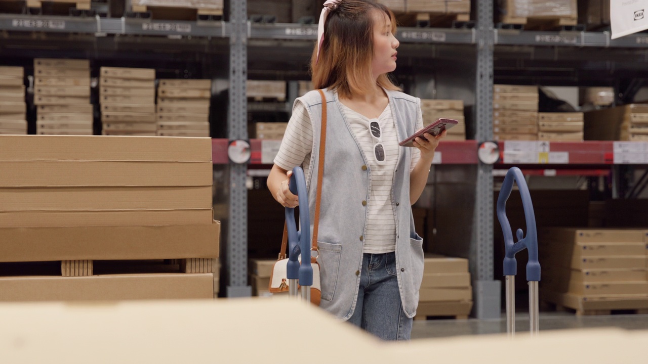 年轻的亚洲女性顾客使用智能手机在零售仓库搜索商品库存。商业仓库购物。视频素材