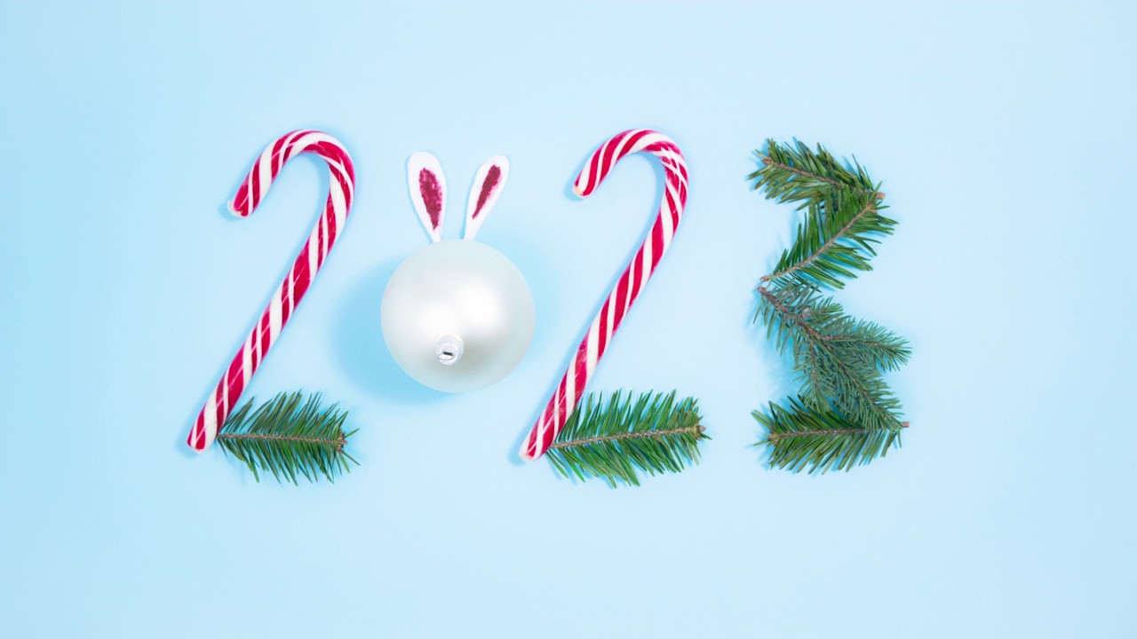 数字2023出现在拐杖糖、白色圣诞球和云杉树枝上。新年的象征。蓝色背景。视频下载