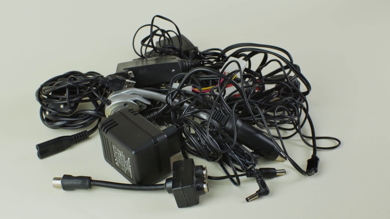 一堆旧的电线，连接和现代设备的充电器在一个明亮的背景特写。一堆旧电线，连接和充电器，孤立的灯光背景。设备过时概念视频下载
