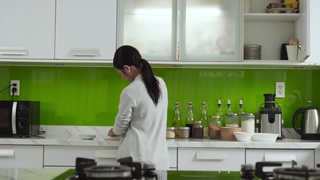 年轻的家庭主妇走在厨房里，把盘子放在橱柜里视频下载