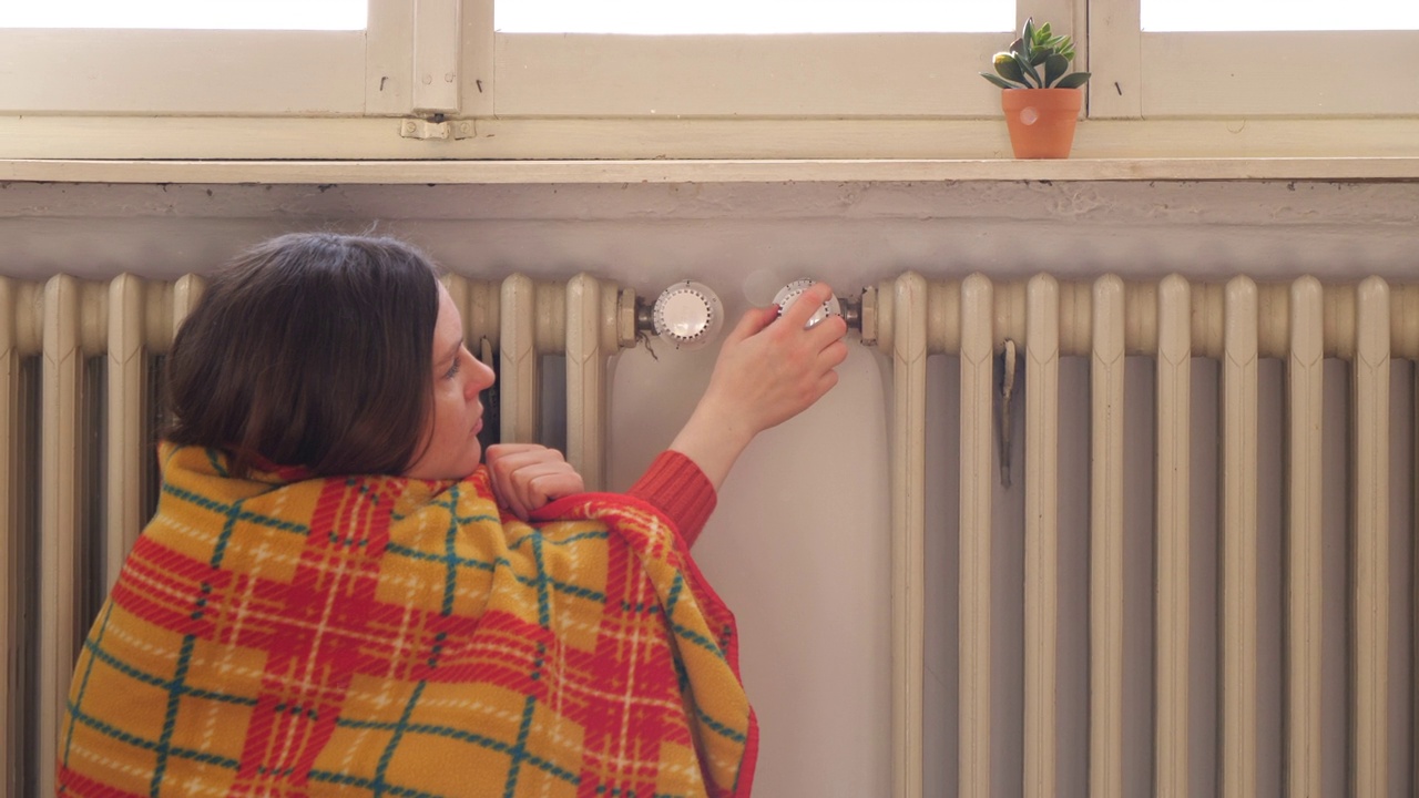 寒冷中的女人在靠近暖气片的毯子下关掉暖气，以节省开支视频下载