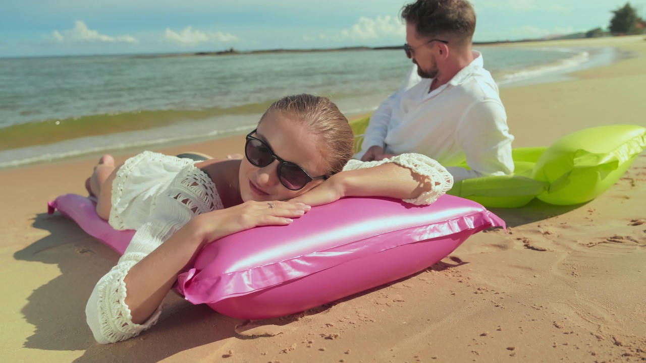 戴着墨镜的女孩在丈夫旁边的充气床垫上晒太阳视频下载