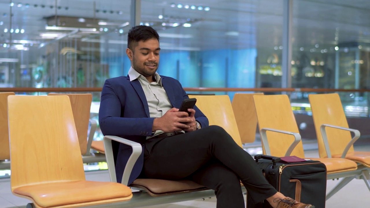一名亚洲商人在机场候机大厅等待时使用手机视频下载