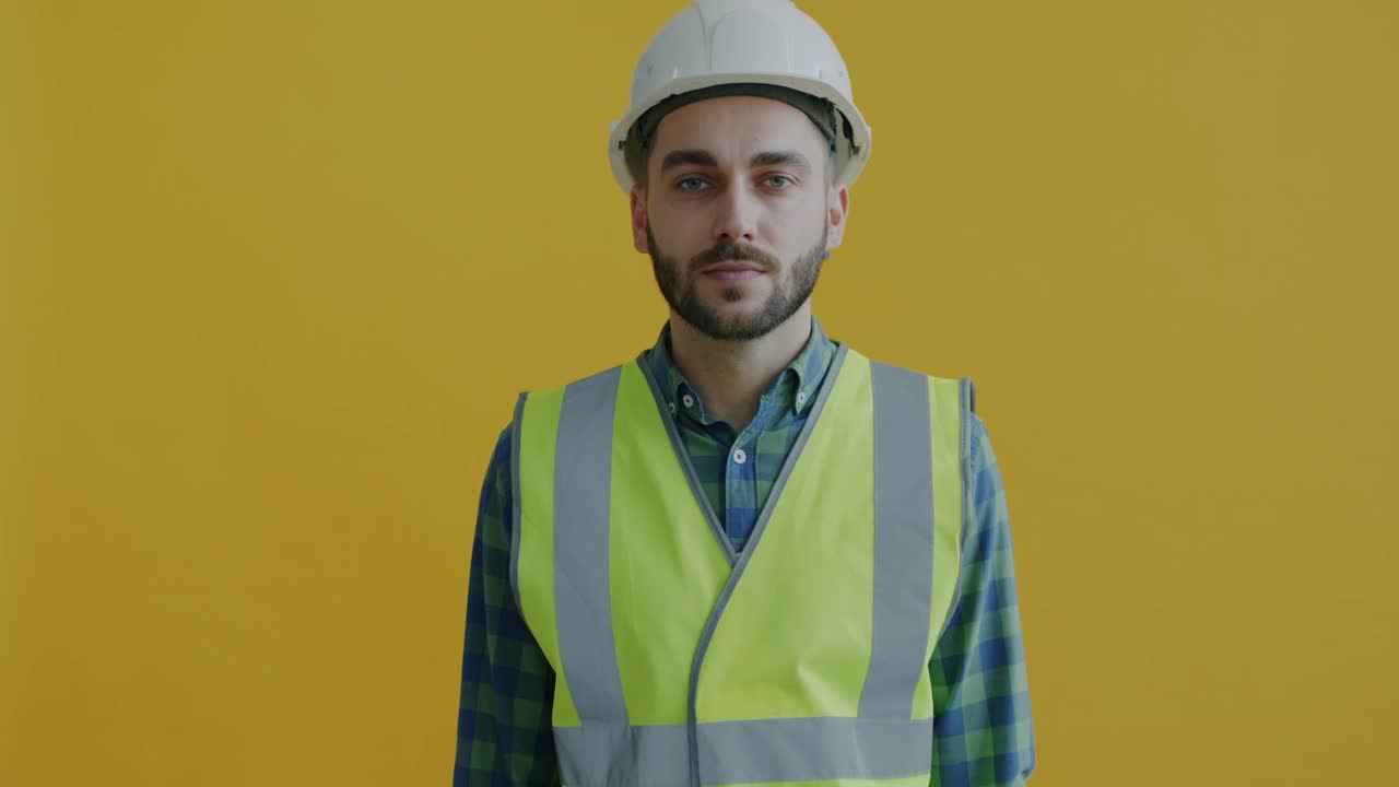 男子在头盔和背心的肖像持有电钻微笑看着相机在黄色背景视频素材